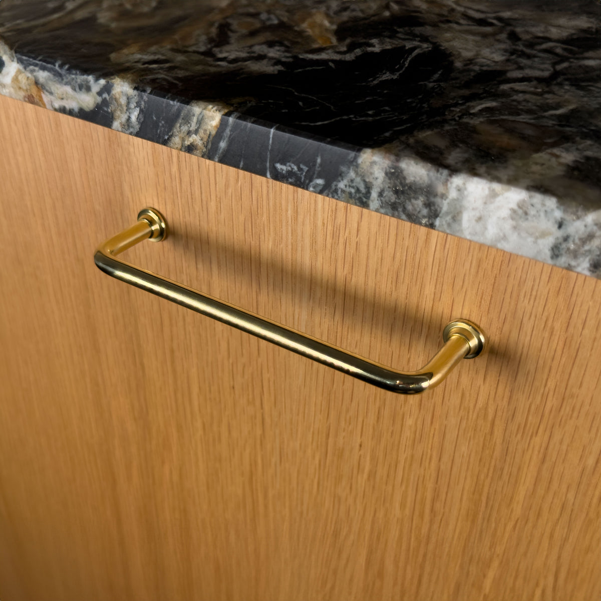 Frederiksberg handle in unlacquered polished brass on a wooden cabinet front, viewed at an angle