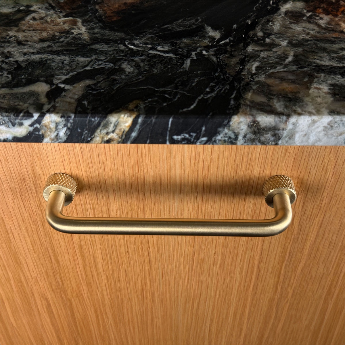Trianglen handle in unlacquered brushed brass with textured roses on a wooden cabinet front, viewed from the front