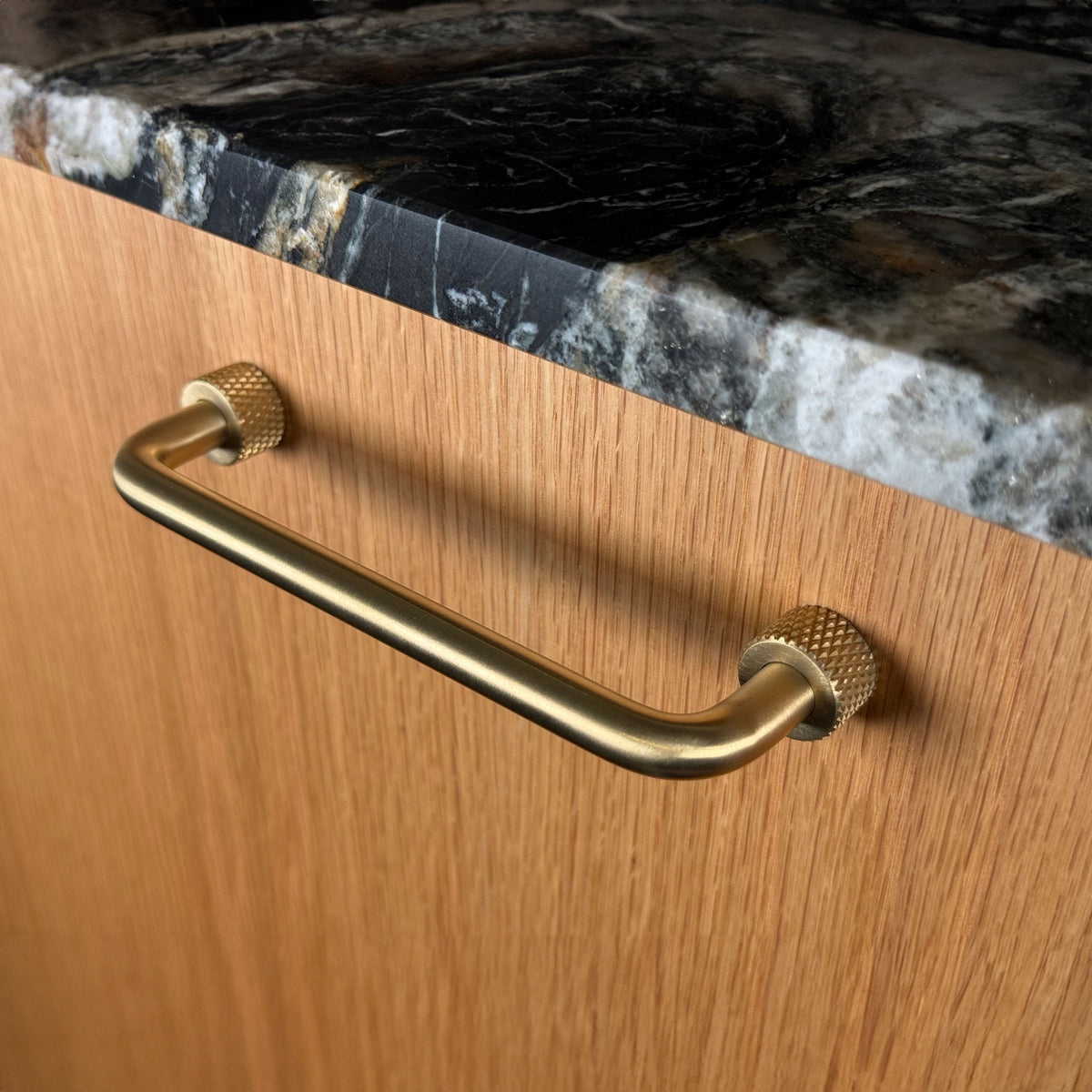 Trianglen handle in unlacquered brushed brass with textured roses on a wooden cabinet front, viewed at an angle