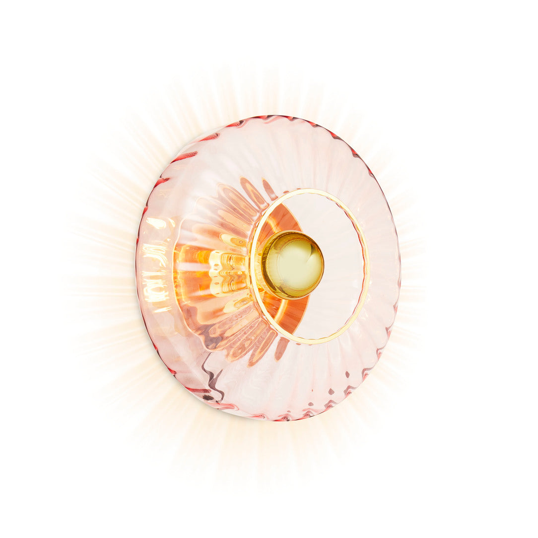 Rund væglampe i rosa plisseret glas, som skaber et lysspil på væggen.