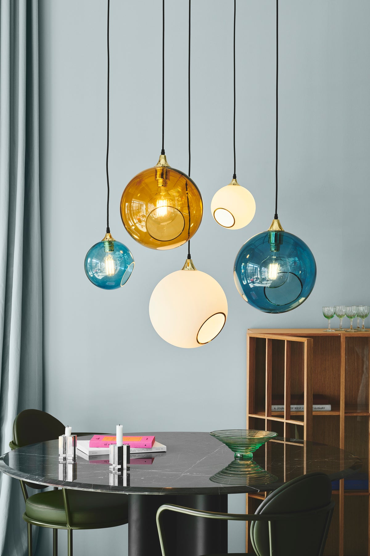 Rund lampe i blåt glas og med et afskåret stykke med guldkant og kig til pæren. Fatning og rosetten er guldfarvet og ledningen er af sort stof.