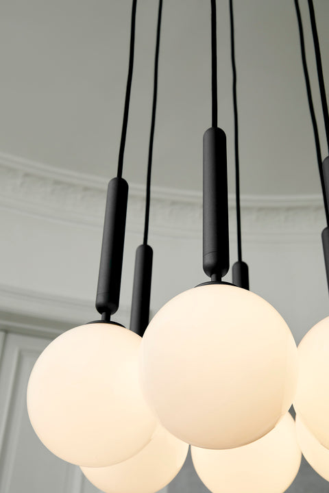 Pendel bestående af seks runde skærme af opalglas med gråt ophæng og sort ledning. Her ses lampen helt tæt på.